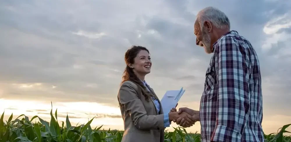 Mulher apertando a mão de fazendeiro em meio a plantação