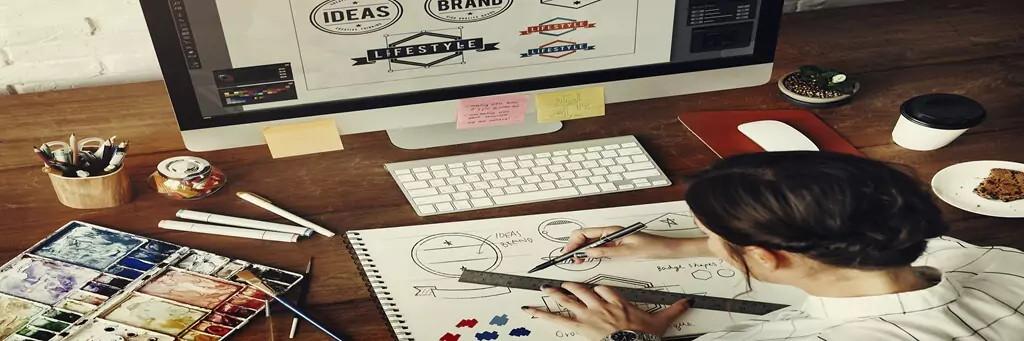 Moça trabalhando em projeto de logo em papel e no computador