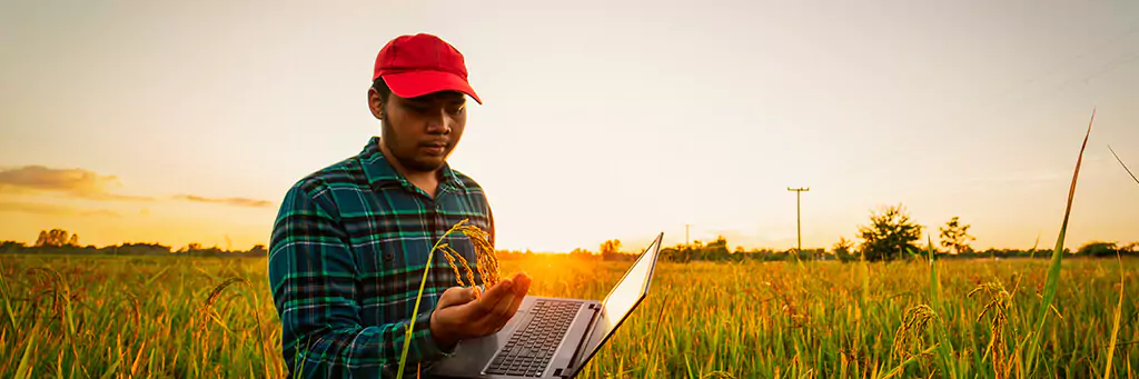 Rapaz em plantação segurando laptop