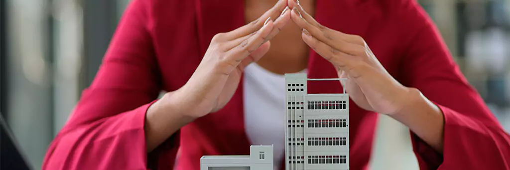 moça colocando mãos em cima de maquete de prédio como proteção