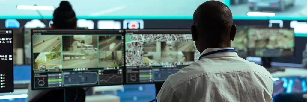 homem em central de seguranca verificando câmeras
